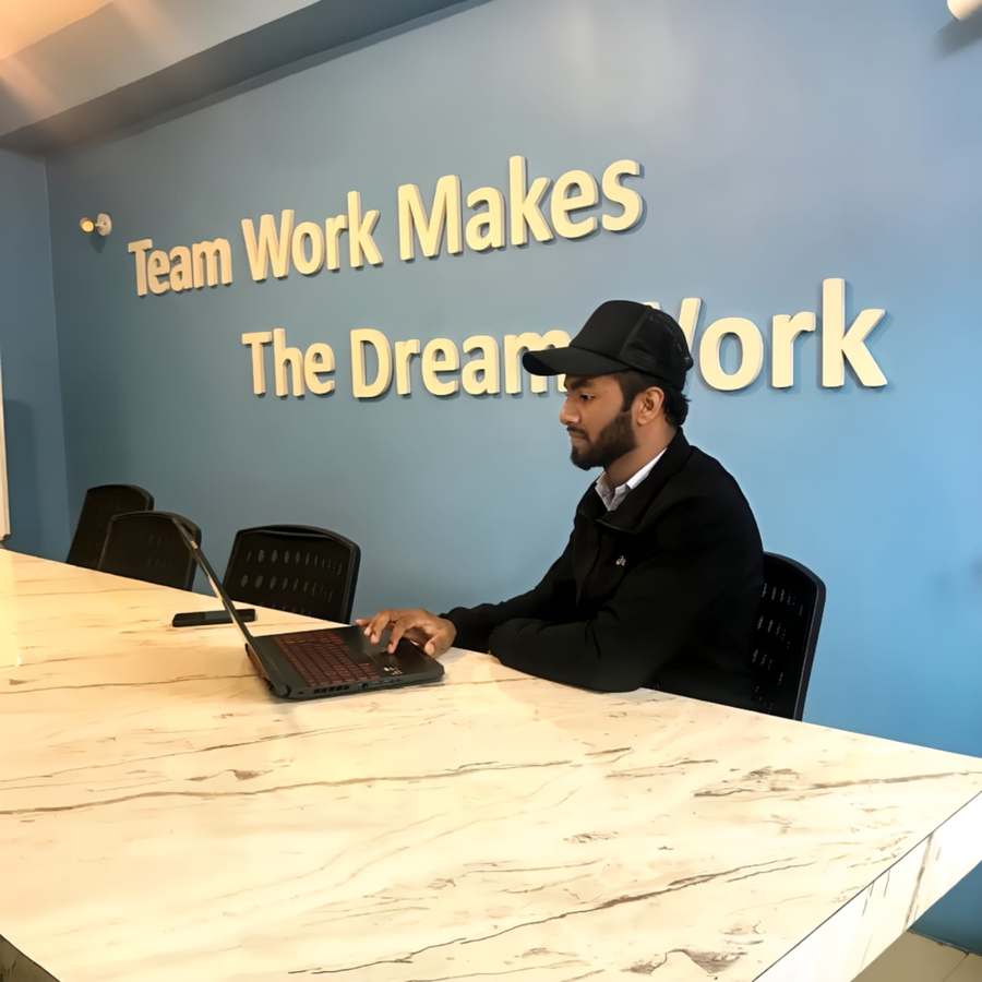Aryan Miya Mansoor working at his laptop under a 'Team Work Makes The Dream Work' sign, SEO expert in Nepal